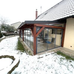 Alt text: Realizace rámového zasklení PLUS v barvě antracit RAL 7016 na dřevěné pergole u rodinného domu.