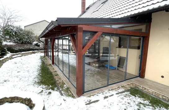 Alt text: Realizace rámového zasklení PLUS v barvě antracit RAL 7016 na dřevěné pergole u rodinného domu.